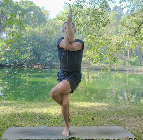 Peter conducting an Iyengar yoga pose outdoors on a yoga mat near a lake