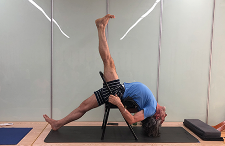Peter balancing himself on a yoga class chair on a yoga mat